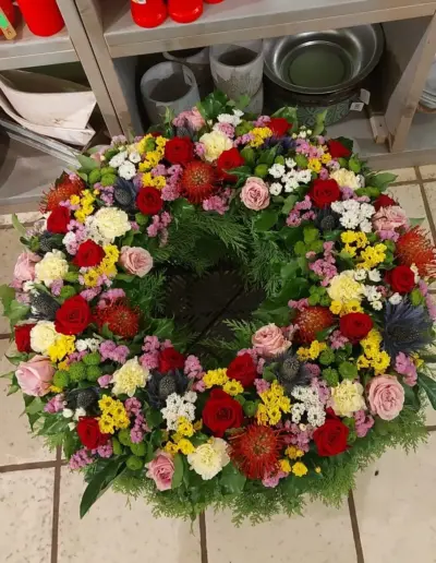 Bunter Trauerkranz mit roten und rosafarbenen Rosen, weißen und gelben Blüten sowie grünem Beiwerk