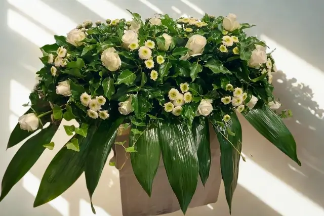 Grabgesteck mit weißen Rosen, kleinen weißen Blüten und dekorativem Grün