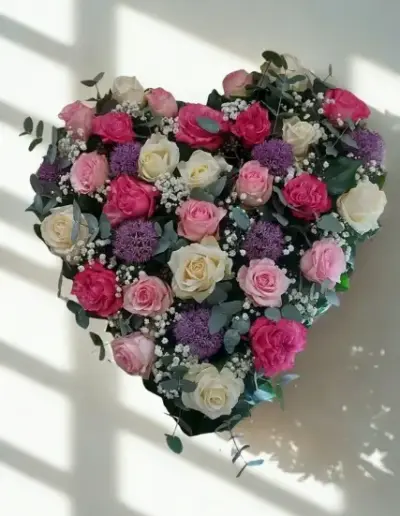 Herzförmiges Trauergesteck mit rosa und weißen Rosen und violetten Blüten