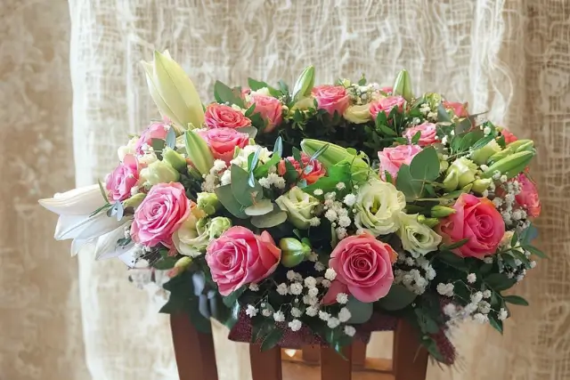 Trauergesteck mit rosa Rosen, weißen Lilien, Schleierkraut und Eukalyptus.
