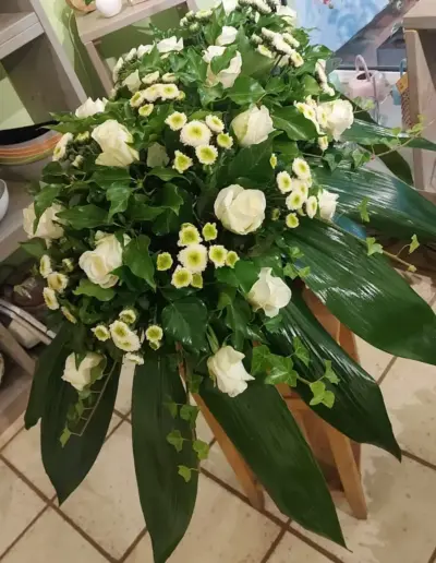 Trauergesteck mit weißen Rosen, kleinen weißen Blüten, Efeu und großen grünen Blättern.