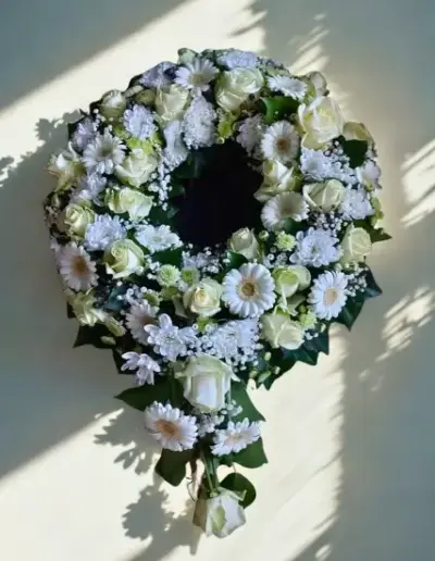 Herzförmiges Trauergesteck mit Rosen in Orange und Creme, Nelken und bunten Blüten auf grünem Blattschmuck.