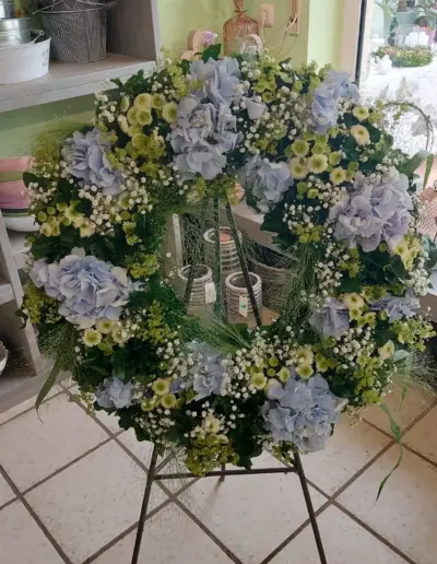 Trauerkranz mit hellblauen Hortensien, kleinen weißen und grünen Blüten sowie grünem Beiwerk.