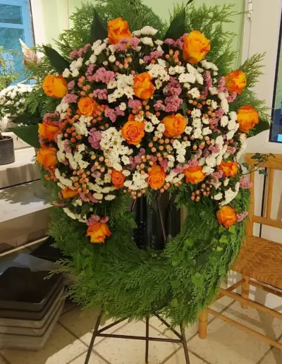 Trauerkranz mit orangefarbenen Rosen, weißen und rosafarbenen Blüten sowie dichtem Grün von der Gärtnerei Ohlemeyer.