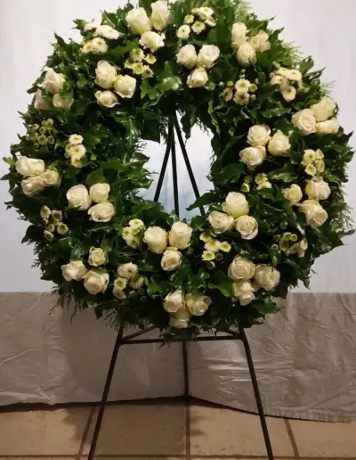 Trauerkranz mit weißen Rosen, kleinen weißen Blüten und dichtem grünem Beiwerk.