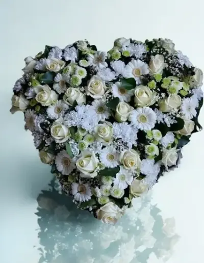 Herzförmiges Trauergesteck mit weißen Rosen, Gerbera, Chrysanthemen und zartgrünen Blüten.