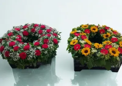 Herzförmiges Trauergesteck mit Rosen in Orange und Creme, Nelken und bunten Blüten auf grünem Blattschmuck.