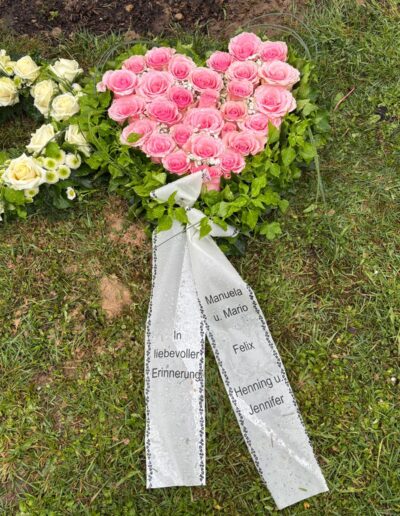 Herzförmiges Trauergesteck aus rosa Rosen mit Trauerschleife