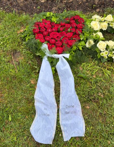 Herzförmiges Trauergesteck aus roten Rosen mit Trauerschleife