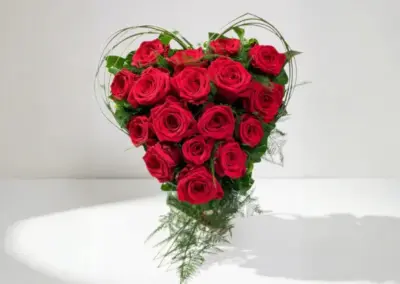 Herzförmiges Blumengesteck aus roten Rosen mit dekorativem Grün