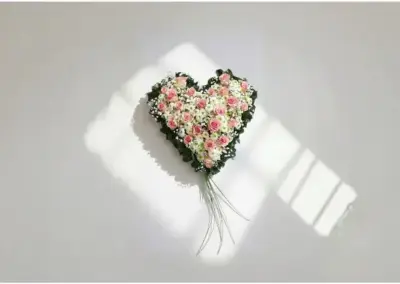 Herzförmiges Blumengesteck mit rosa und weißen Rosen und dekorativem Grün