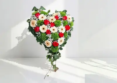 Herzförmiges Blumengesteck mit roten Rosen, weißen Gerbera, grünen Blüten und Schleierkraut
