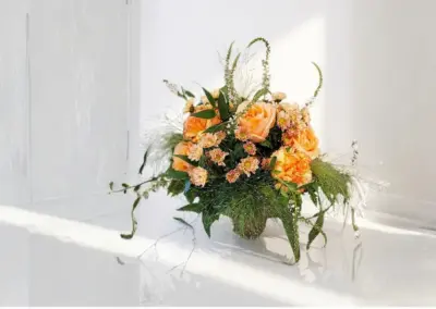 Oranges Blumengesteck mit Rosen, Nelken und lockerem grünem Beiwerk